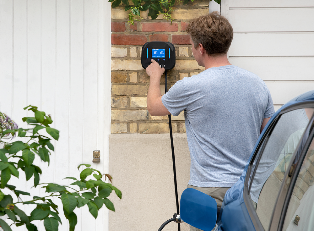 Man operating Ohme Home Pro EV charger LCD screen while charging electric vehicle on driveway